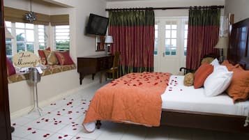 A bedroom with a bed, a desk, a television, and a window with curtains.
