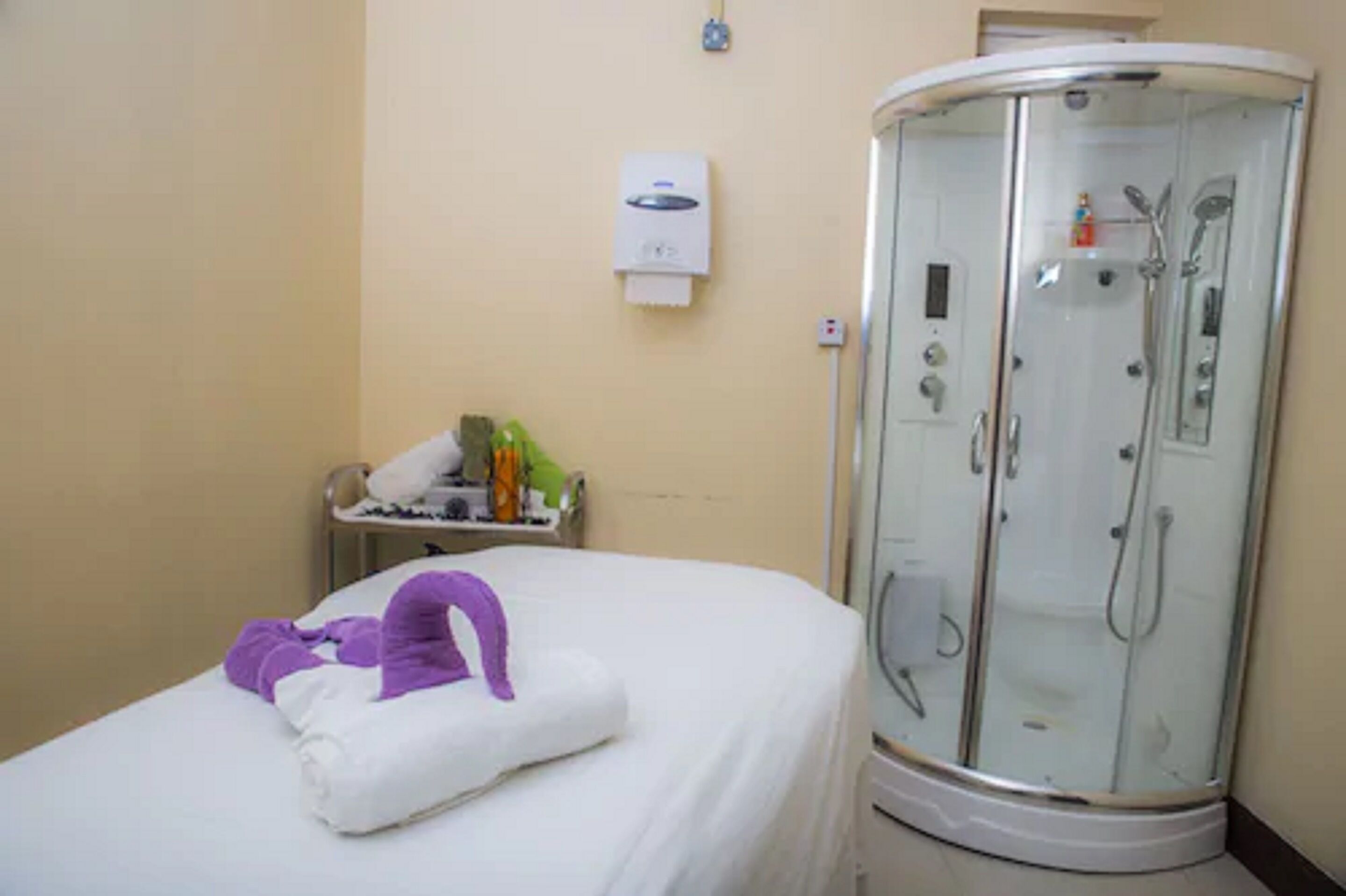 Habitación de hotel con cama, baño con ducha de vidrio y una mesita con artículos de aseo.
