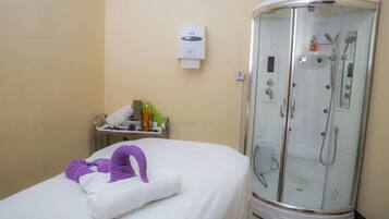 Habitación de hotel con cama, baño con ducha de vidrio y una mesita con artículos de aseo.