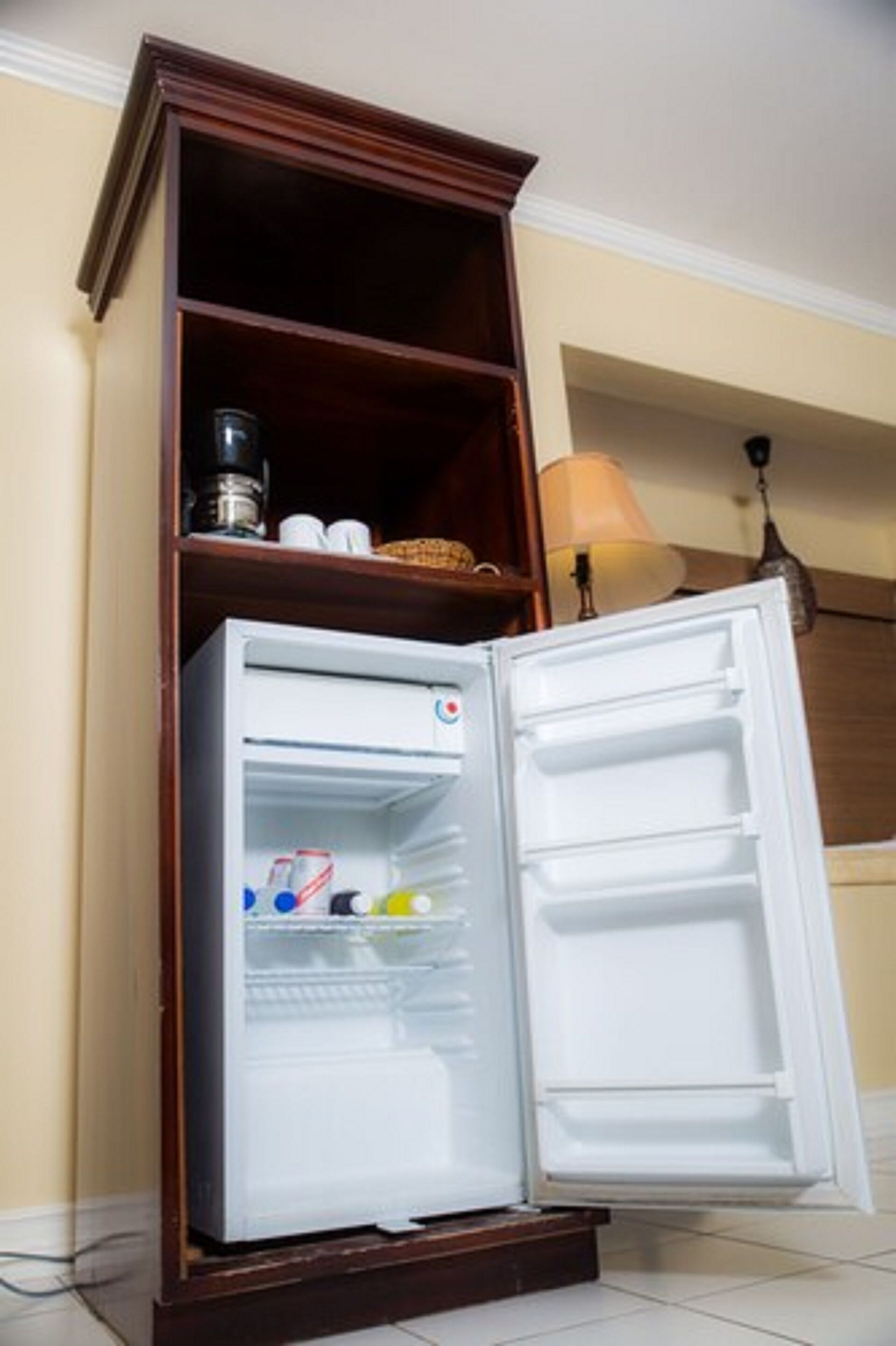 A white refrigerator with a wooden shelf above it, containing a coffee maker and cups.