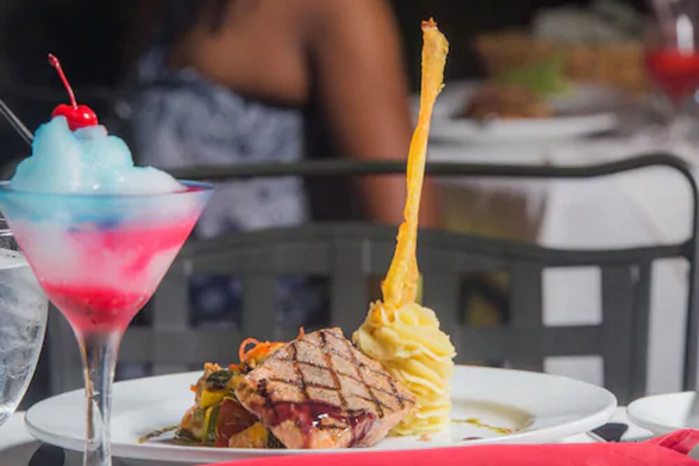 A dessert with a cherry on top, a tall drink with a cherry, and a plate with food and a tall, thin item.