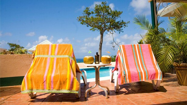 Dos sillones con toallas a rayas, una mesa de billar y una palmera en un entorno exterior soleado.