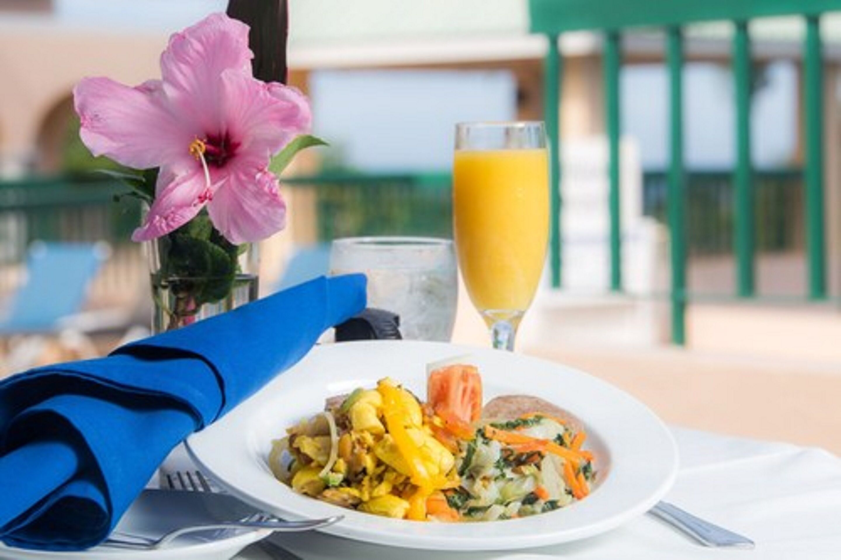 A breakfast setting with a plate of food, a glass of orange juice, and a pink flower.