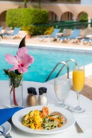 Uma mesa de jantar com um prato de comida, um copo de suco de laranja e um vaso de flores perto de uma piscina.