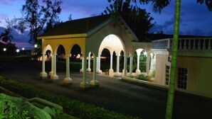 Un edificio con un paseo techado y columnas, rodeado de vegetación.