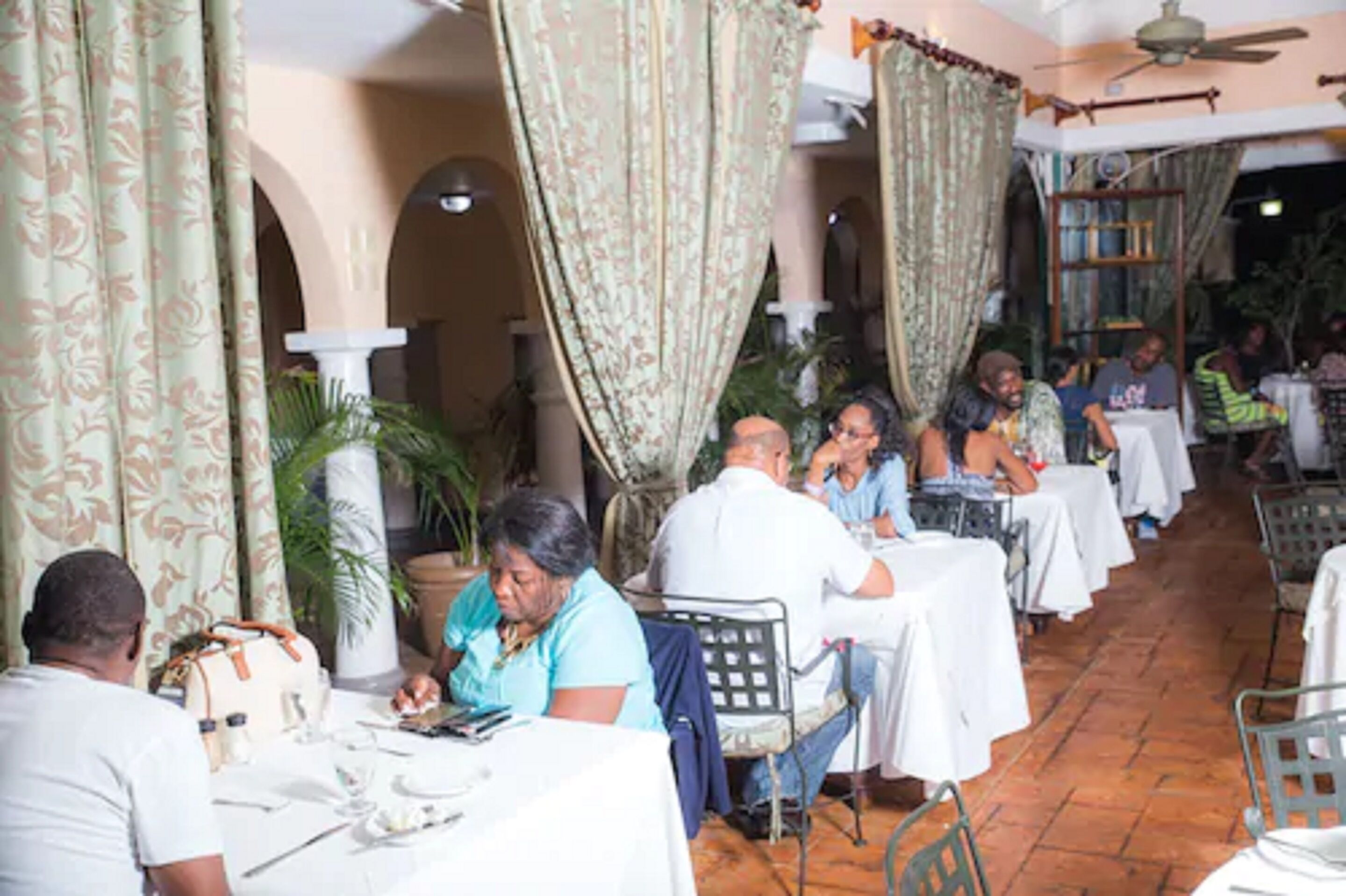 Een restaurant met tafels, stoelen, etende mensen en een plafondventilator.