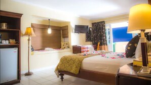 Habitación de hotel con cama, mesita de noche, lámpara, televisor y un refrigerador pequeño.