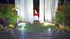 Un patio al aire libre con un arreglo circular de asientos, cortinas blancas y una mesa con mantel rojo.