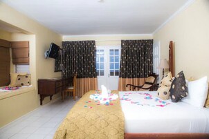 Quarto de hotel com cama, escrivaninha, cadeira, televisão e cortinas.