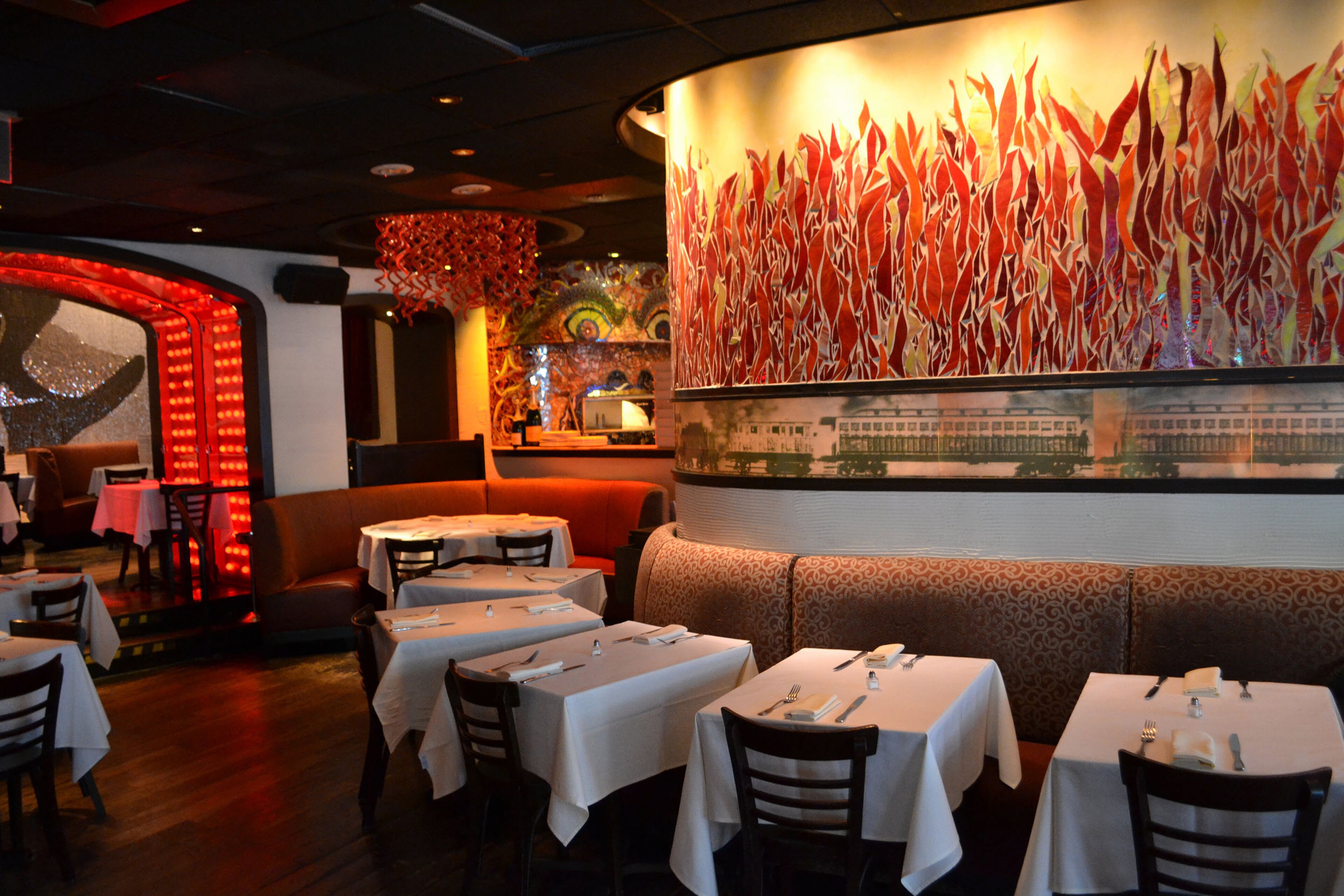 A restaurant interior with booths, tables, and a large abstract painting on the wall.
