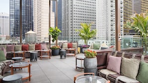 A rooftop lounge with outdoor seating, potted plants, and a city view.