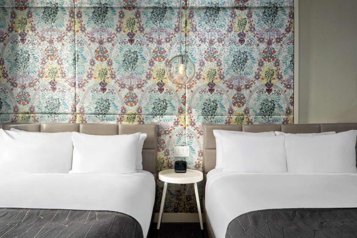 Camera d'albergo con due letti, un comodino con una sveglia e una decorazione a parete.