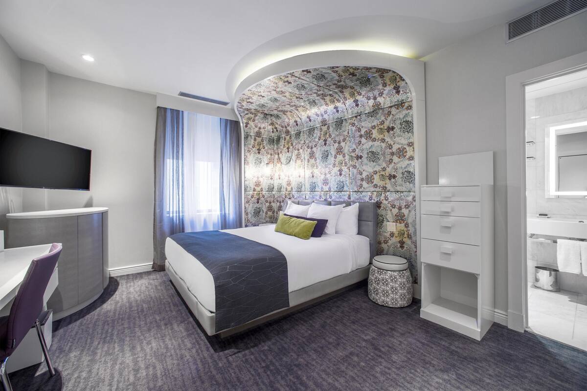 Una camera d'albergo moderna con un letto, una scrivania, una TV, un bagno e una zona doccia.