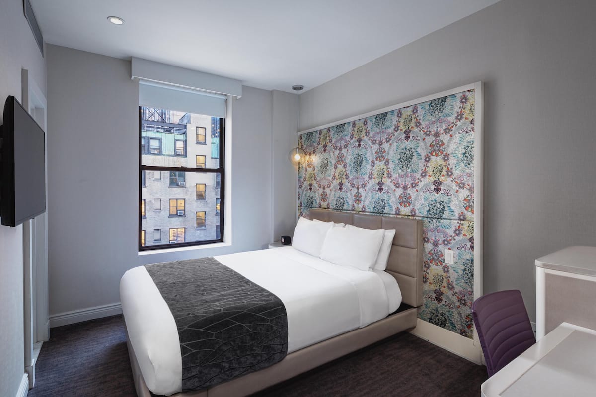 Una moderna camera d'albergo con un letto grande, una finestra vista città, una testiera decorativa e una piccola scrivania.