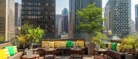 Terraza en la azotea con sofá, sillas y plantas en macetas, con vistas a un paisaje urbano con edificios altos.