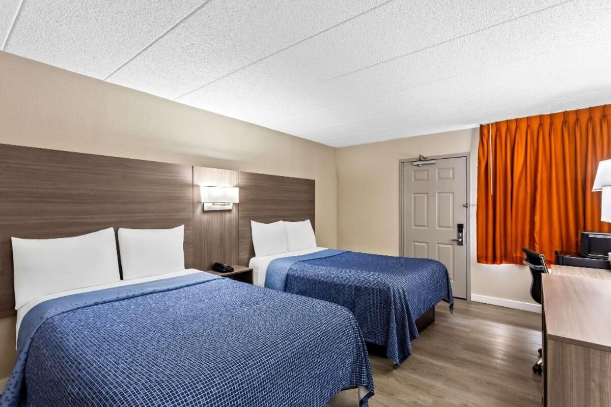A hotel room with two beds, a desk, a chair, and a door.