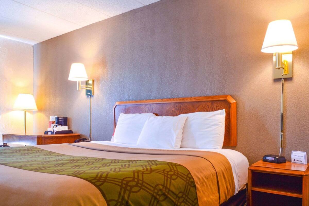 A hotel room with a large bed, two bedside lamps, a nightstand with a coffee maker, and a Thinx sign on the nightstand.