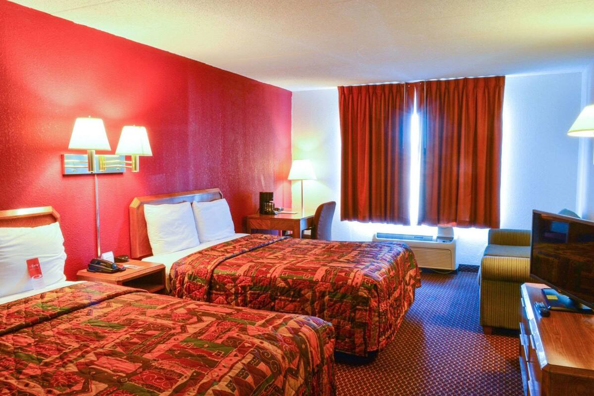 A hotel room with two beds, a desk, a chair, a TV, and a window with curtains.