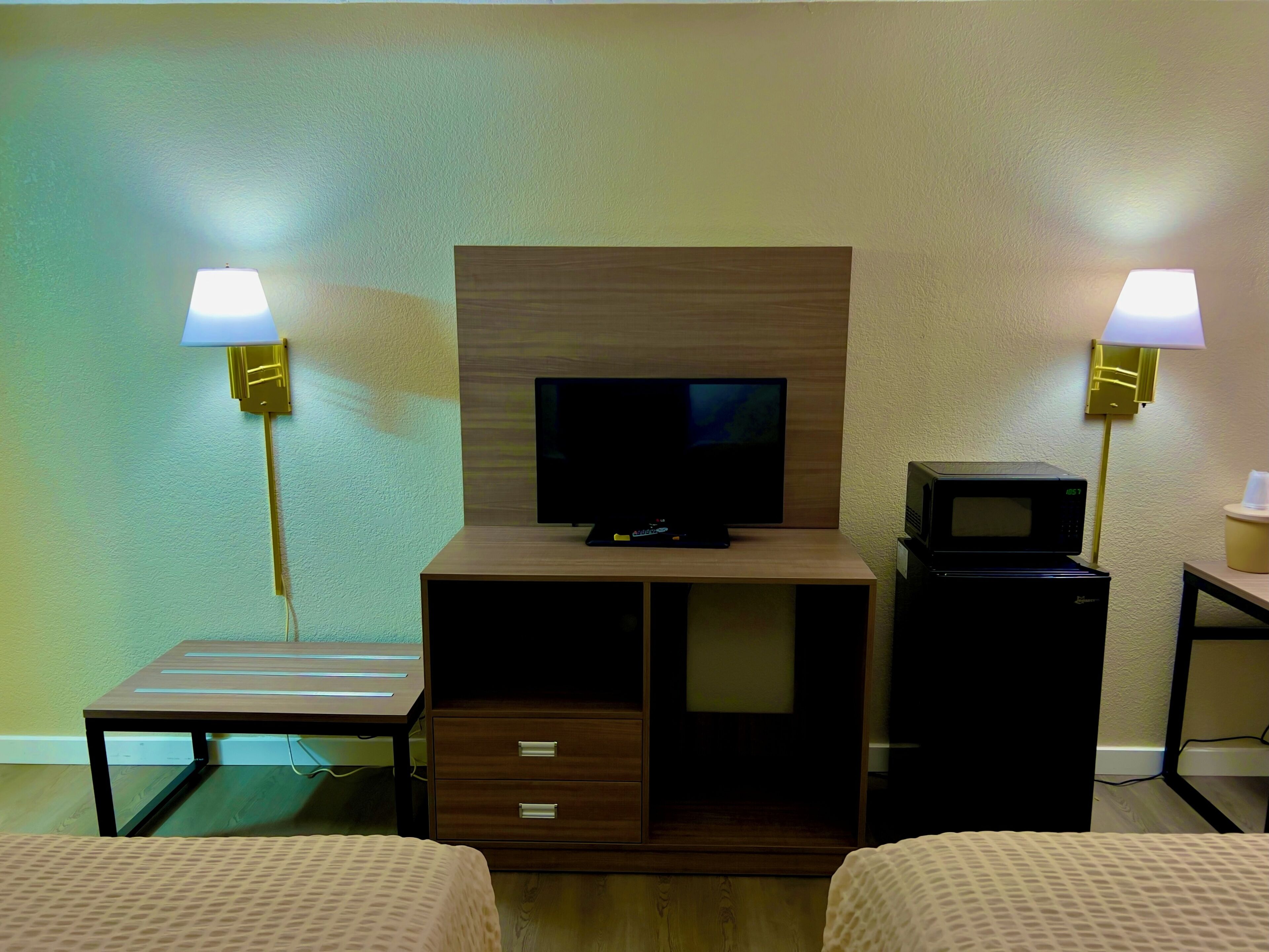 A hotel room with a television, a microwave, two bedside lamps, a small table, and a bed.