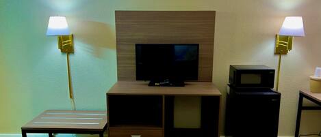 A hotel room with a television, a microwave, two bedside lamps, a small table, and a bed.