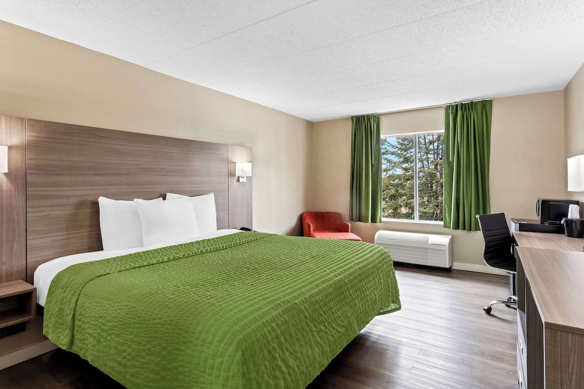 A hotel room with a large bed, a desk, a chair, and a window with curtains.