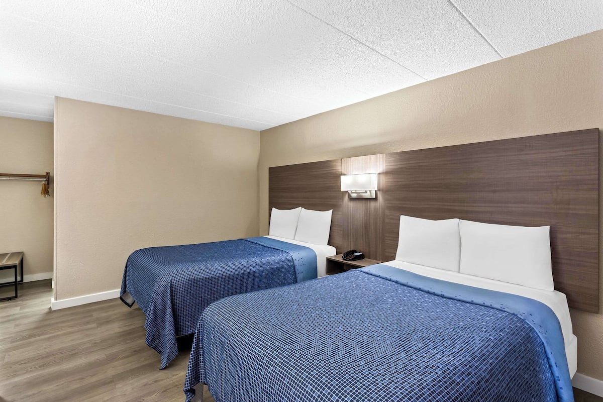 A hotel room with two beds, beige walls, wooden headboard, and a nightstand with a phone.