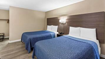 Habitación de hotel con dos camas, paredes color beige, cabecera de madera y mesita de noche con un teléfono.