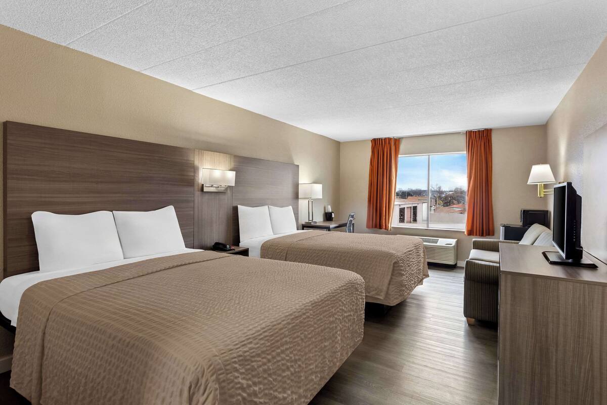 A hotel room with two beds, a desk, a TV, and a window with curtains.