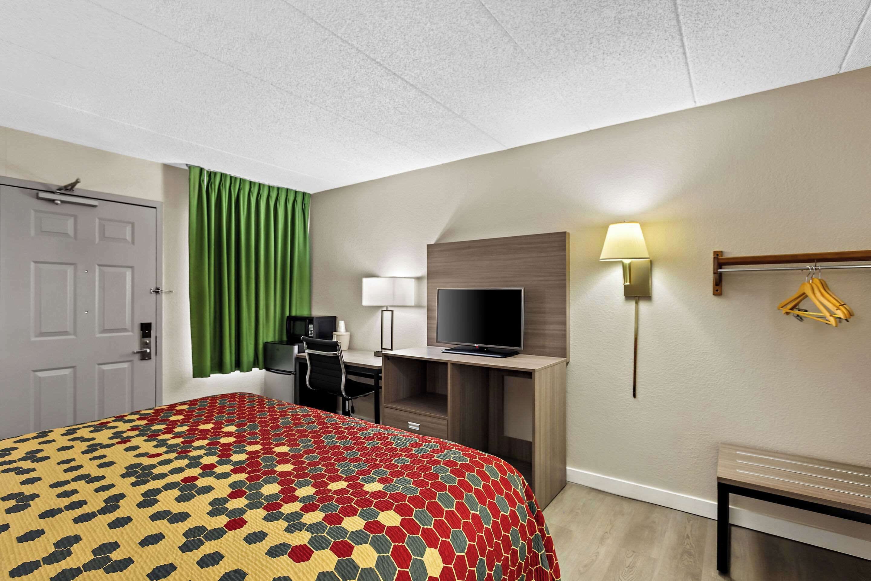 A hotel room with a bed, desk, TV, and a lamp.