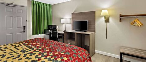 A hotel room with a bed, desk, TV, and a lamp.