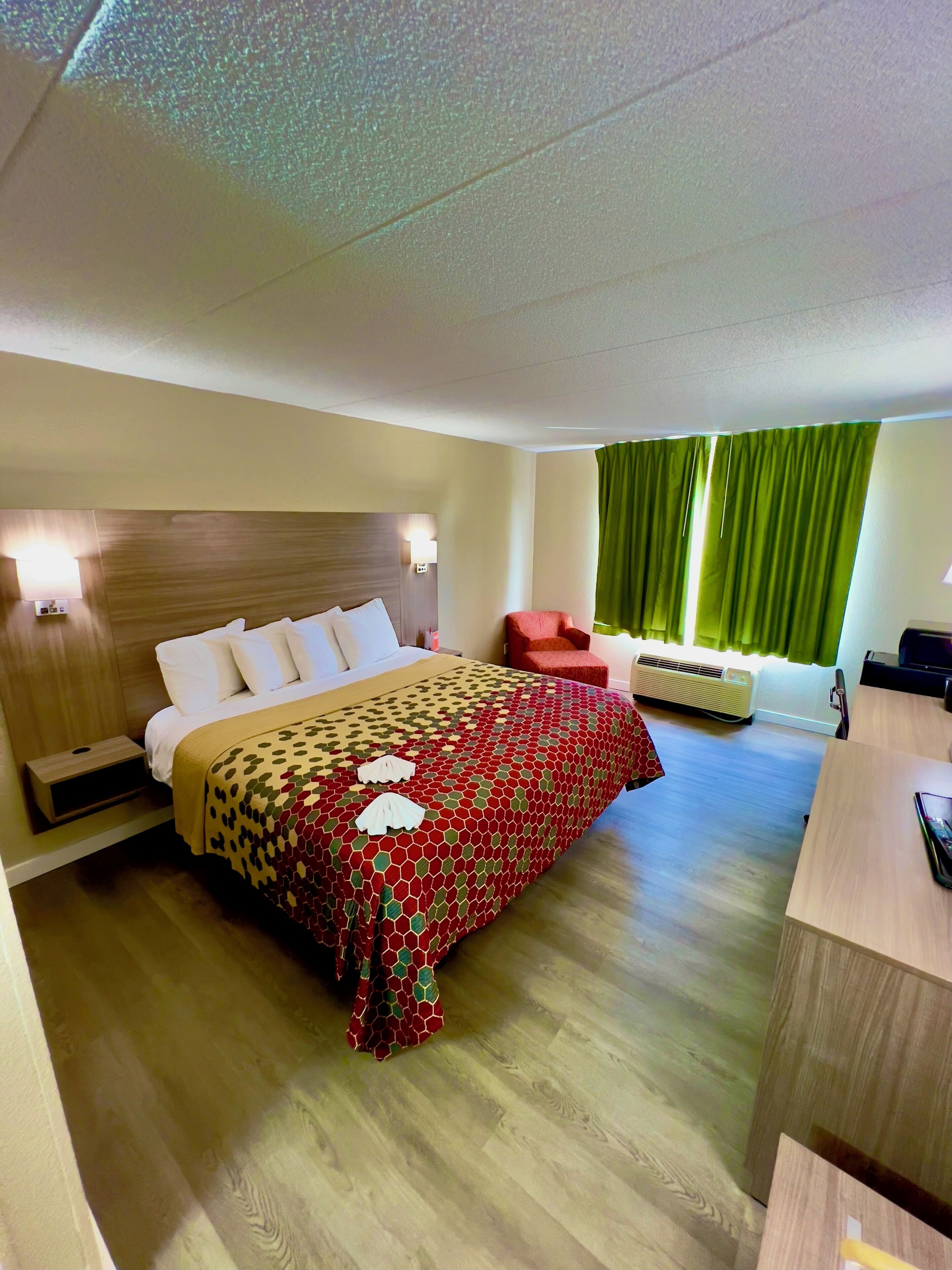 Hotelkamer met een bed, nachtkastjes, een bureau, een stoel, een verwarming en een raam met gordijnen.