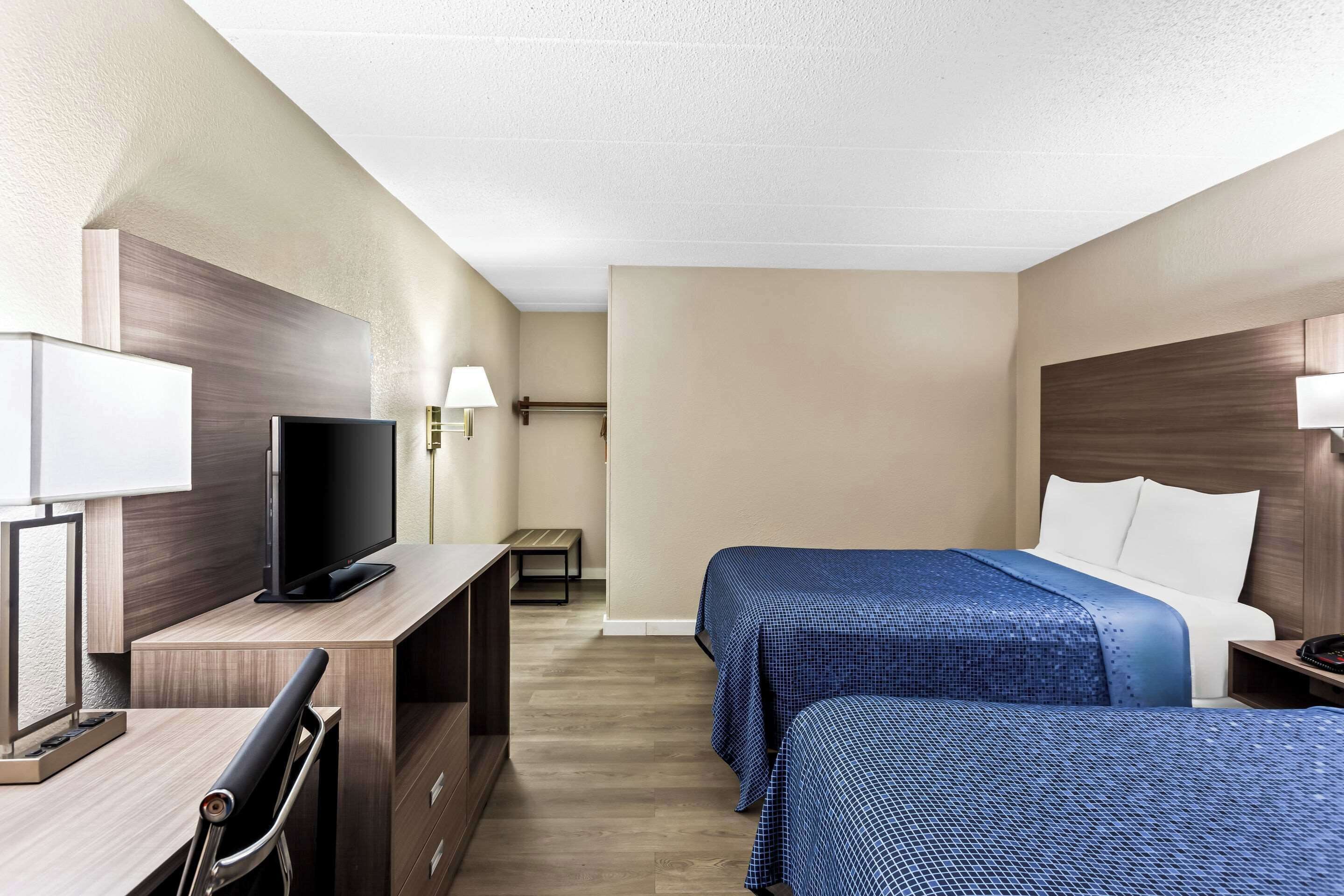 Habitación de hotel con escritorio, televisión, dos camas y mesita de noche.