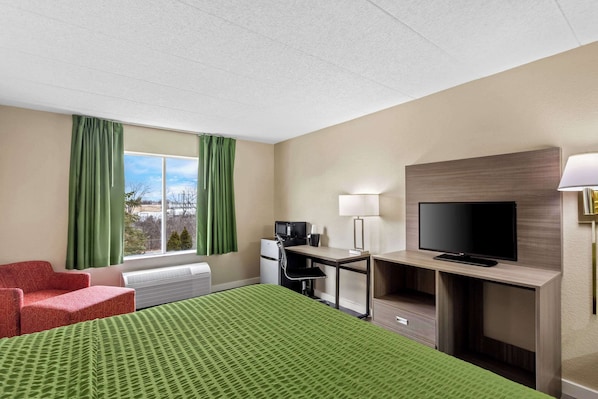 A hotel room with a bed, a desk, a television, a chair, and a window with curtains.