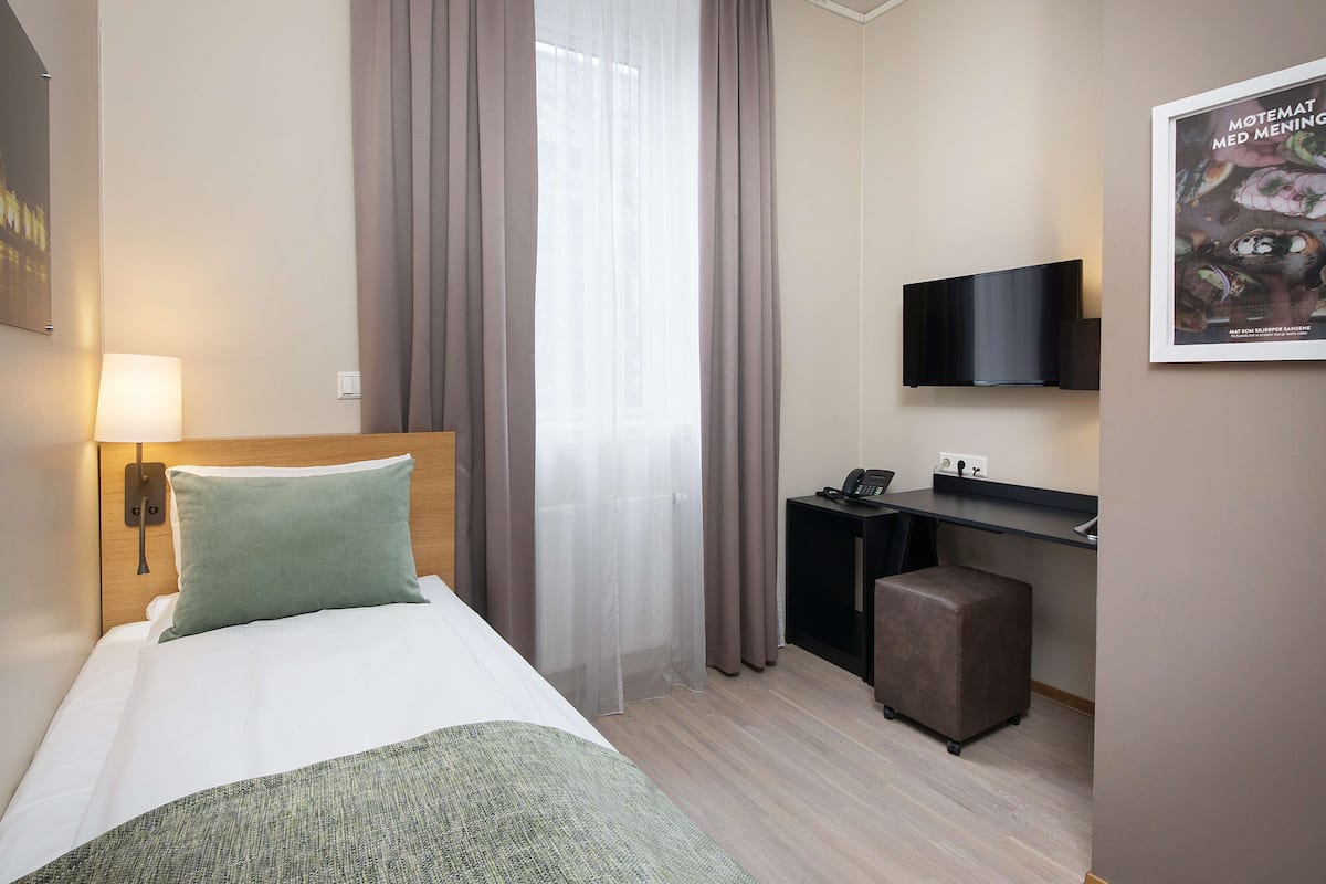 Una habitación de hotel con cama, escritorio, televisor y un pequeño otoman.