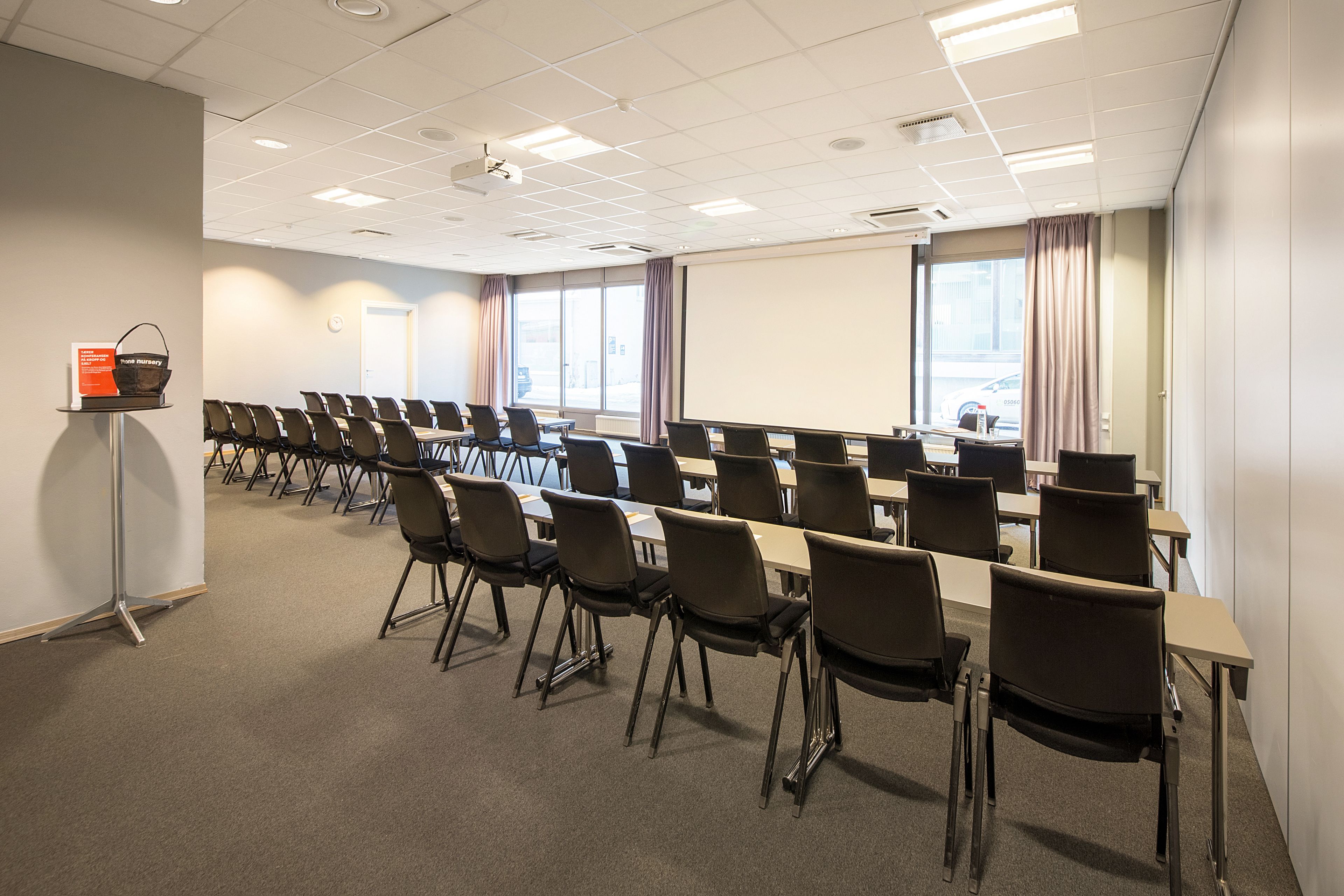 Un salón de conferencias con filas de sillas, un proyector y una pantalla.