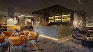 Een moderne hotellobby met een bar, lederen zitplaatsen en een behang met patroon.