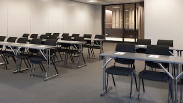 A conference room with rows of tables and chairs, a large screen, and a glass partition with curtains.