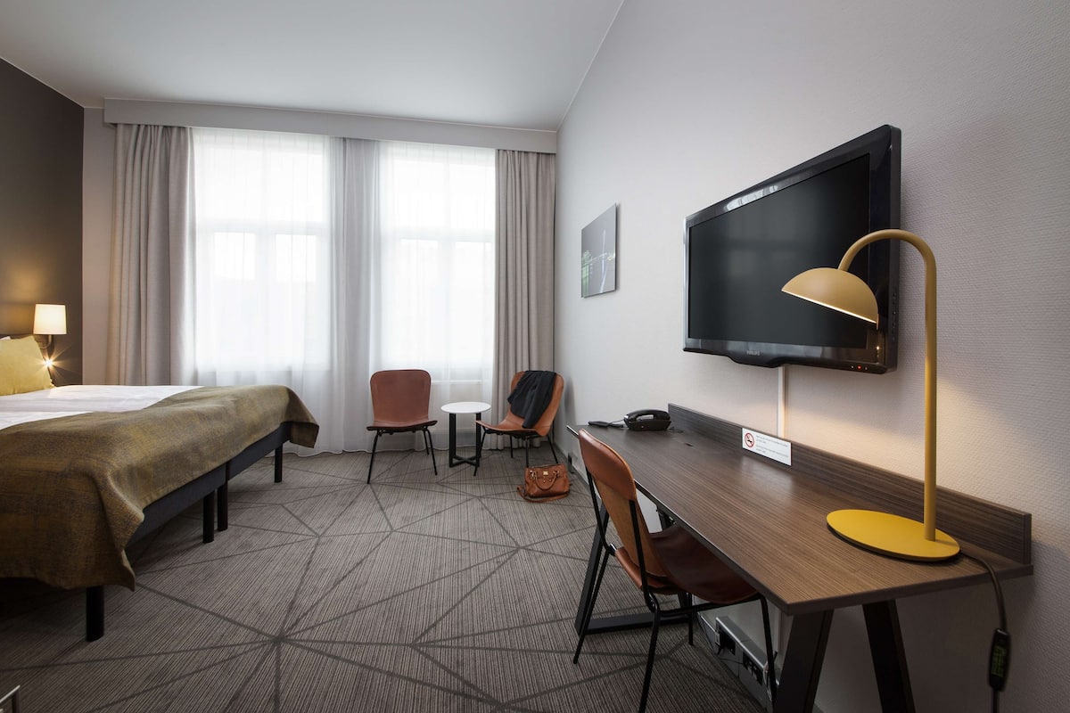 Una habitación de hotel con una cama, un escritorio, una silla, un televisor y una lámpara.