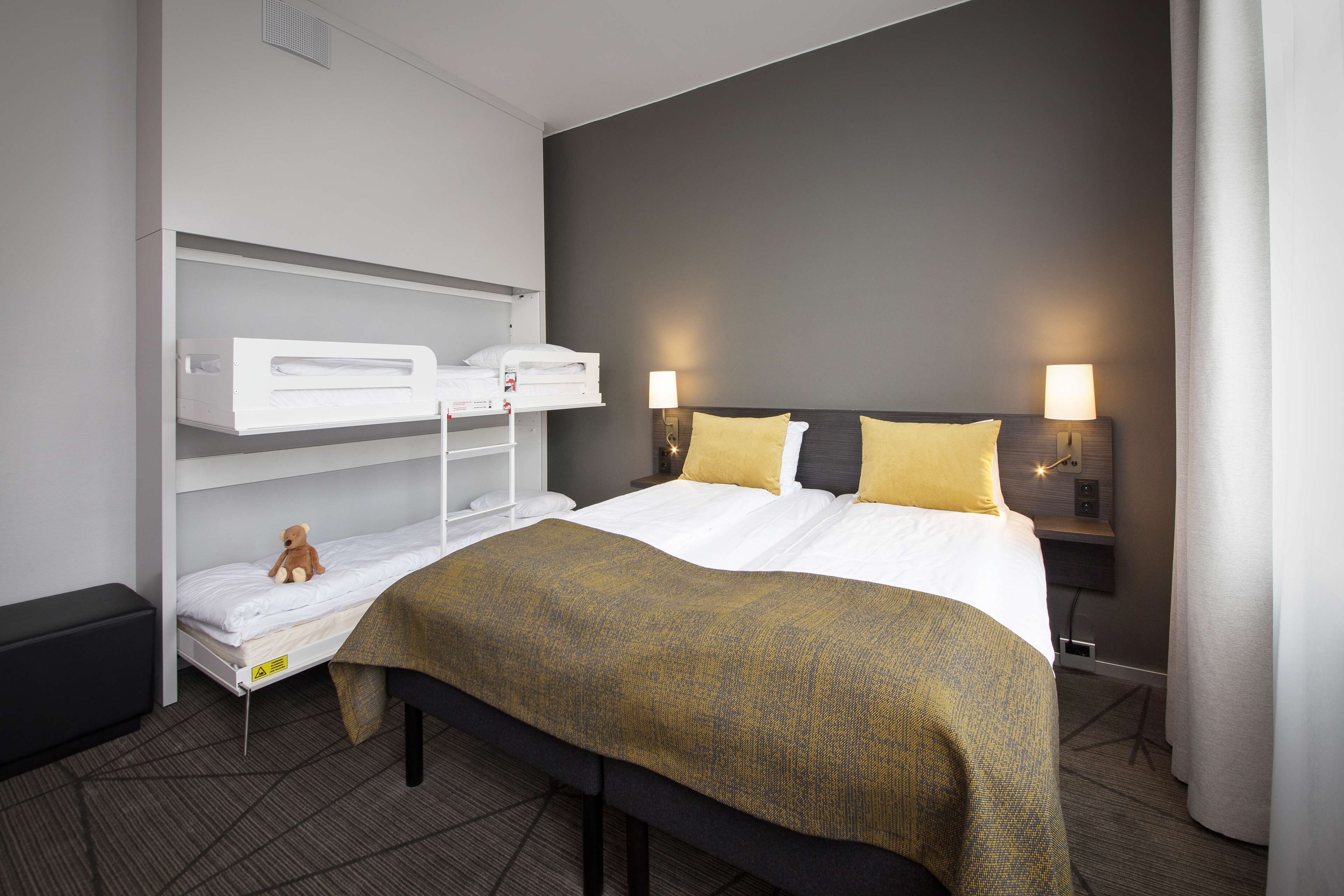 Ein Hotelzimmer mit Etagenbett, Nachttisch mit Lampen und einer Ablage mit Teddybär.