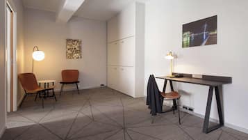 Een moderne kantoorruimte met een geometrisch vloerkleed, twee stoelen, een bureau met een lamp en een ingelijst schilderij aan de muur.