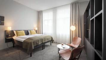 A hotel room with a bed, bedside tables, a chair, a small table, and a window with curtains.