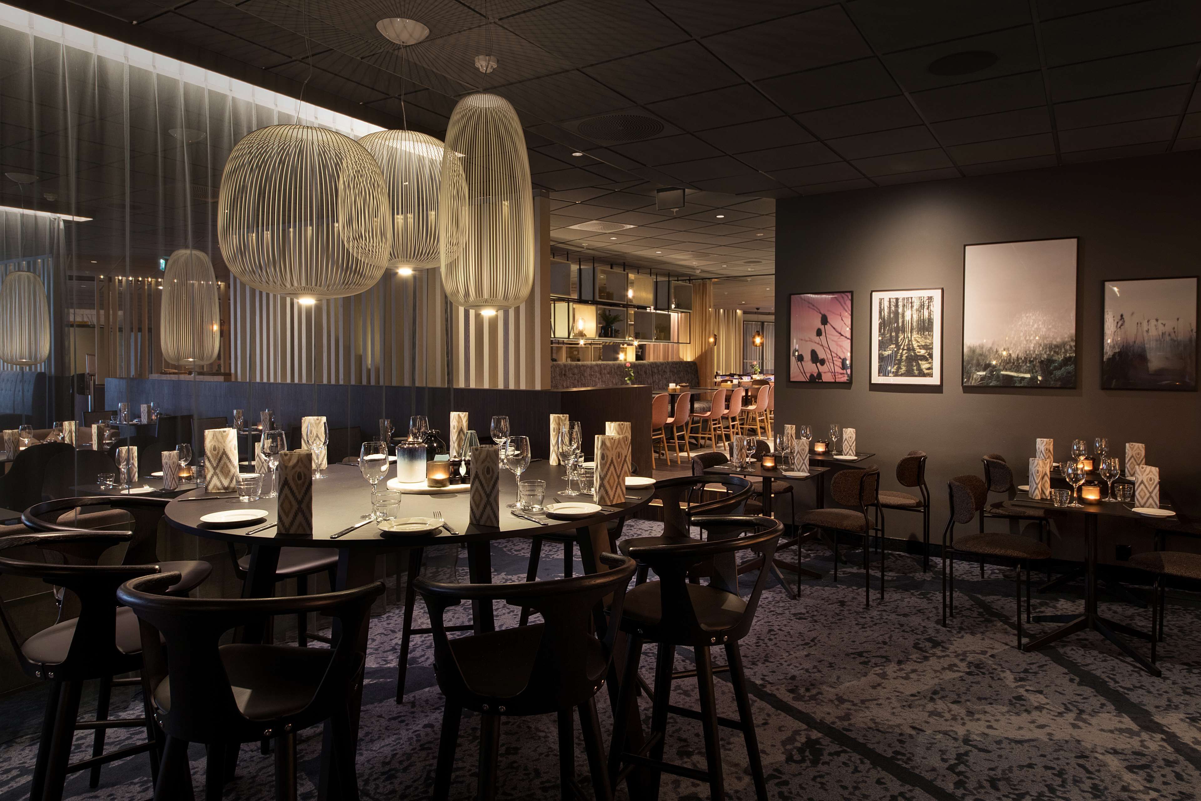 A modern dining area with round tables, dark chairs, and hanging pendant lights.