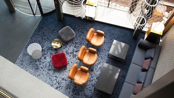 Un área de descanso moderna con alfombra azul, sillones de cuero, un reposapiés rojo y un sofá gris.