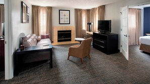 A hotel room with a sofa, armchair, TV, fireplace, and a desk with a lamp. - Residence Inn Syracuse Carrier Circle (East Syracuse)