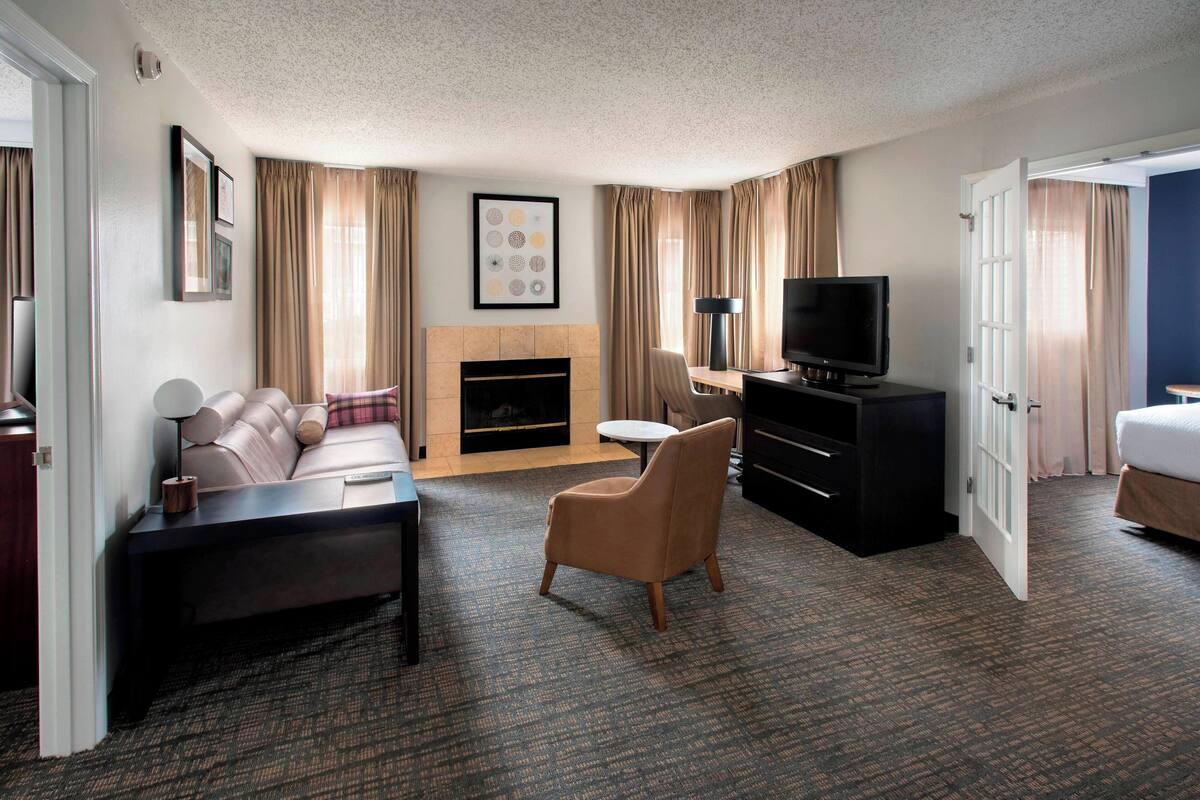 Une chambre d’hôtel équipée d’un canapé, d’un fauteuil, d’une télévision, d’une cheminée et d’un bureau avec une lampe.