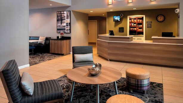 A hotel lobby with a reception desk, a sofa, a round table, and a small stool. - Residence Inn Syracuse Carrier Circle (East Syracuse)
