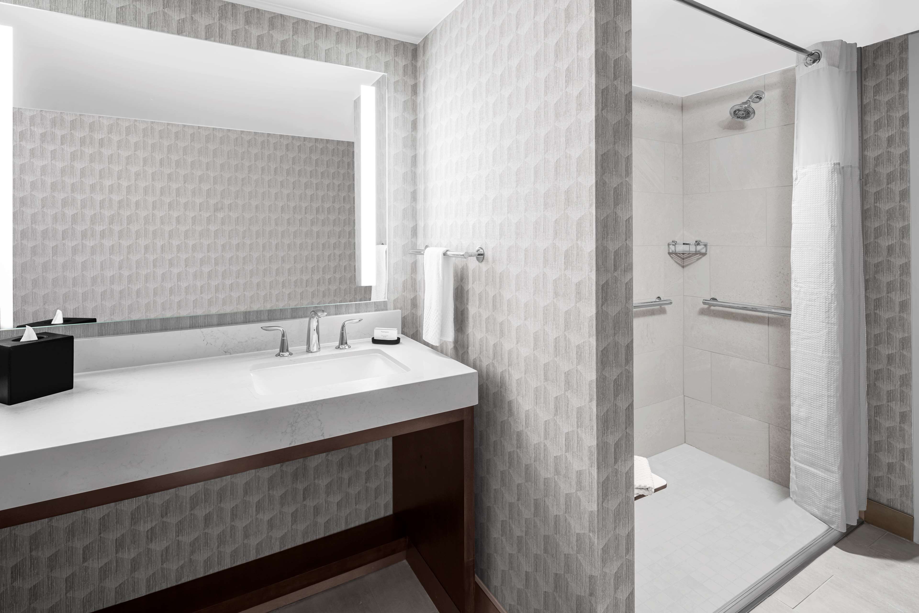 A modern bathroom with a large mirror, a sink, a shower, and a towel rack.
