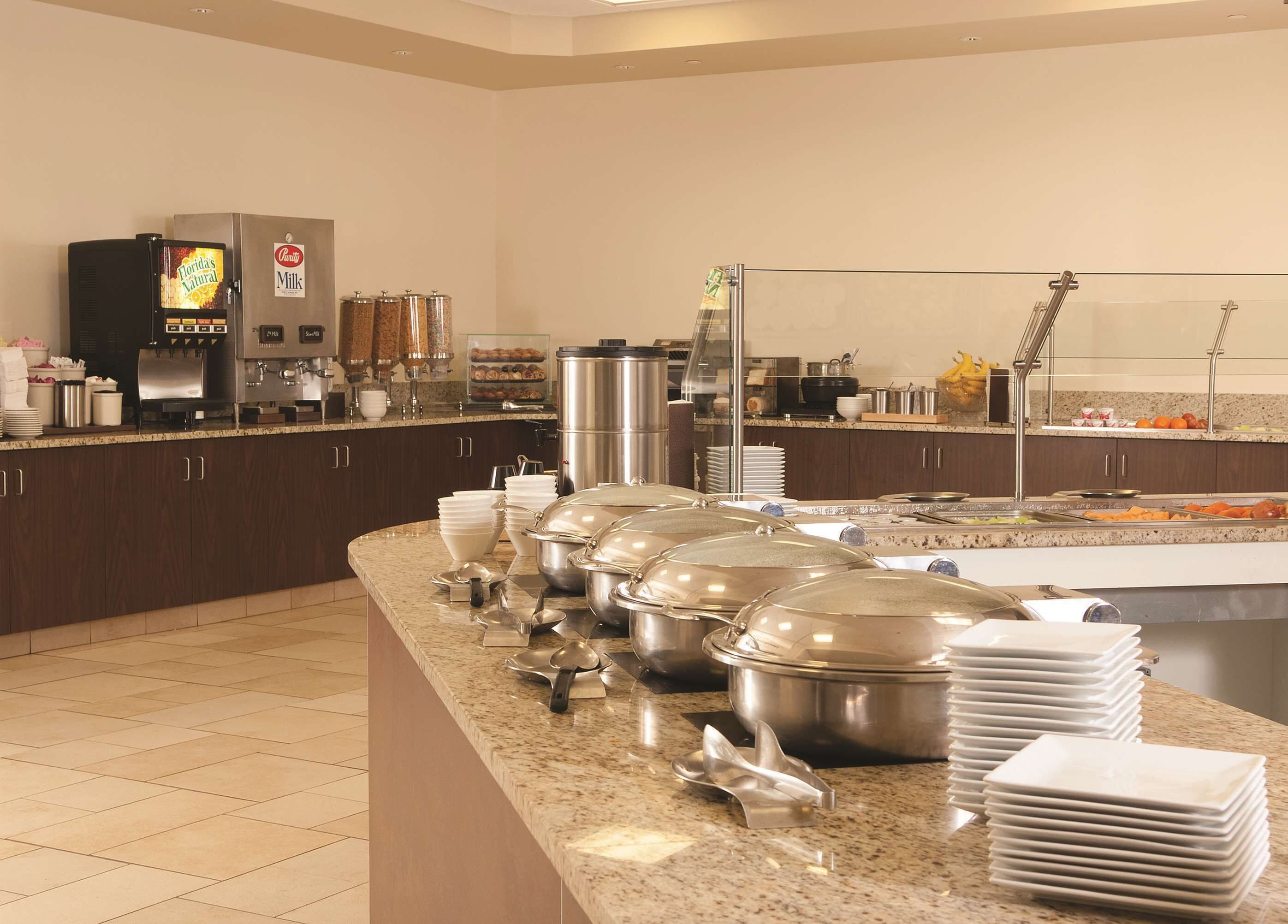 Montaje de bufé con diferentes recipientes de comida, una máquina de café y platos apilados.