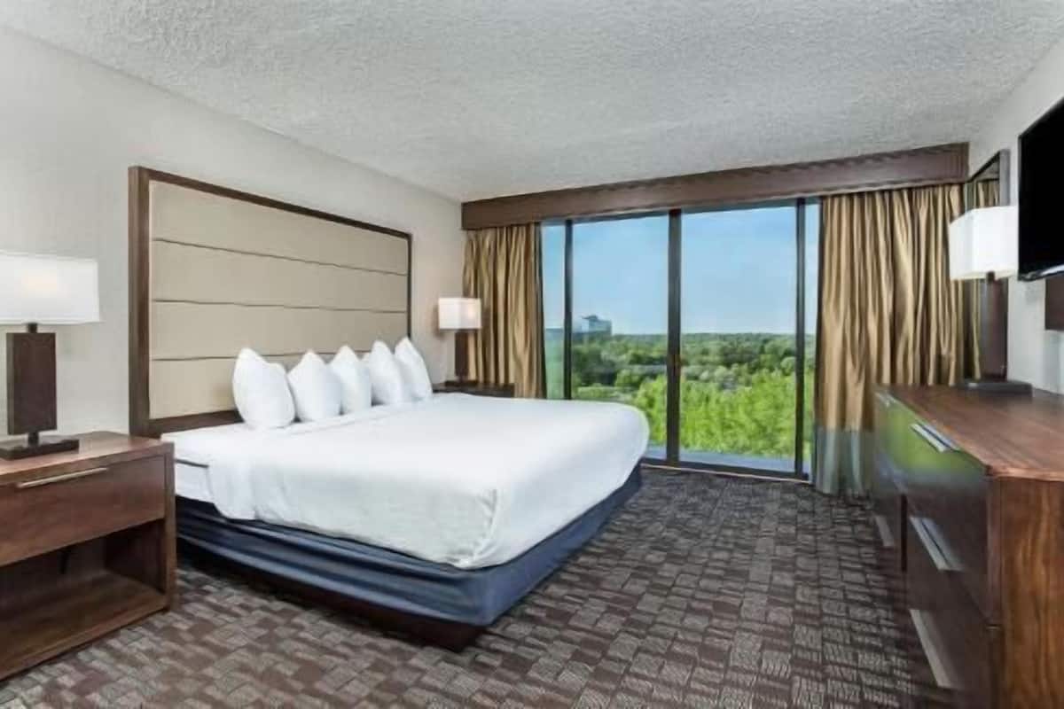 Ein Hotelzimmer mit einem großen Bett, einem Schreibtisch, einem Fernseher und Blick ins Grüne.