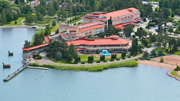 A large, multi-story hotel with a red roof, situated by a lake with a dock and a swimming pool. - Naantali Spa Hotel (Naantali)